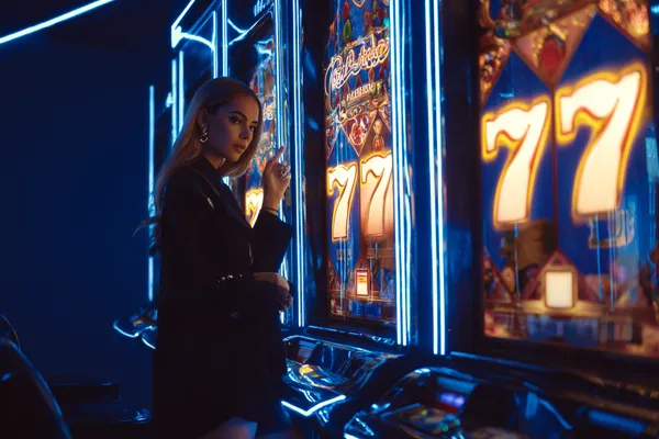 A woman smiling by bright slot machines showing lucky symbols, showcasing the exciting slot offerings at KM787.